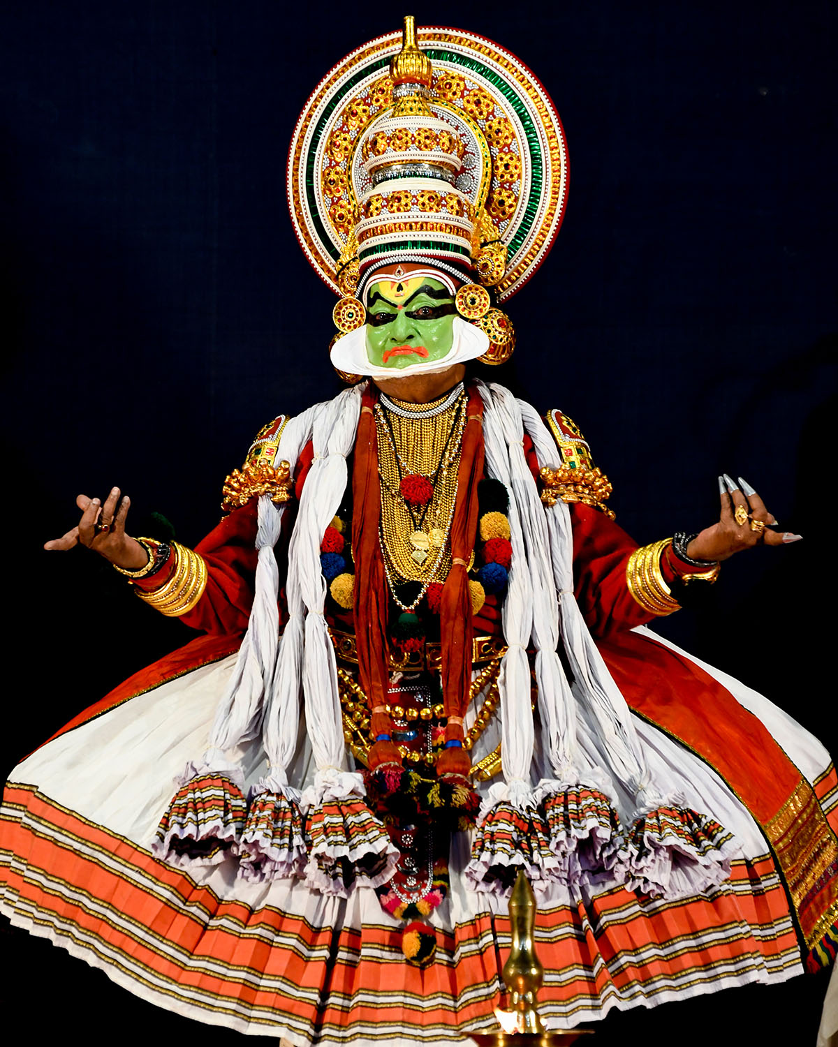 A Kathakali dancer in the costume of a male character with his hands held in a gesture of wondering.