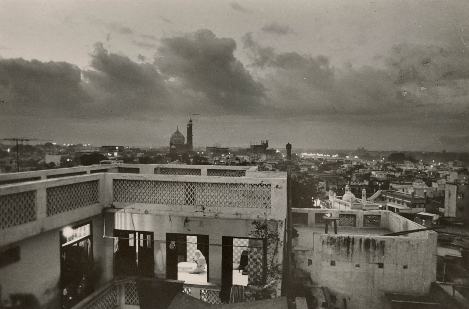 Archival photograph by Raghu Rai of a woman praying inside her home with the Jama Masjid in Delhi in the backdrop