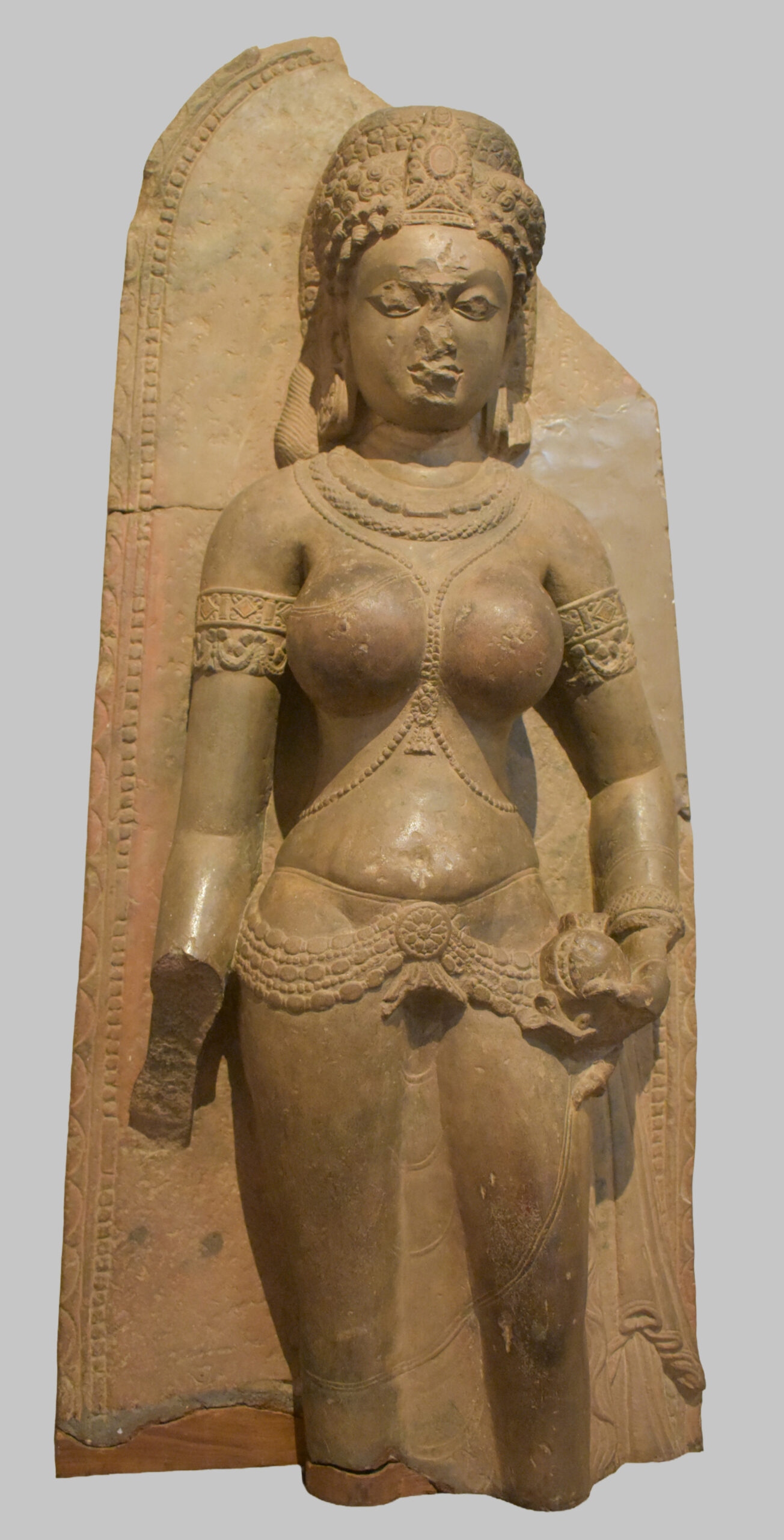 Photograph of a standing sandstone Tara from Sarnath with its right hand broken and left hand holding a circular object dated to the 11th century