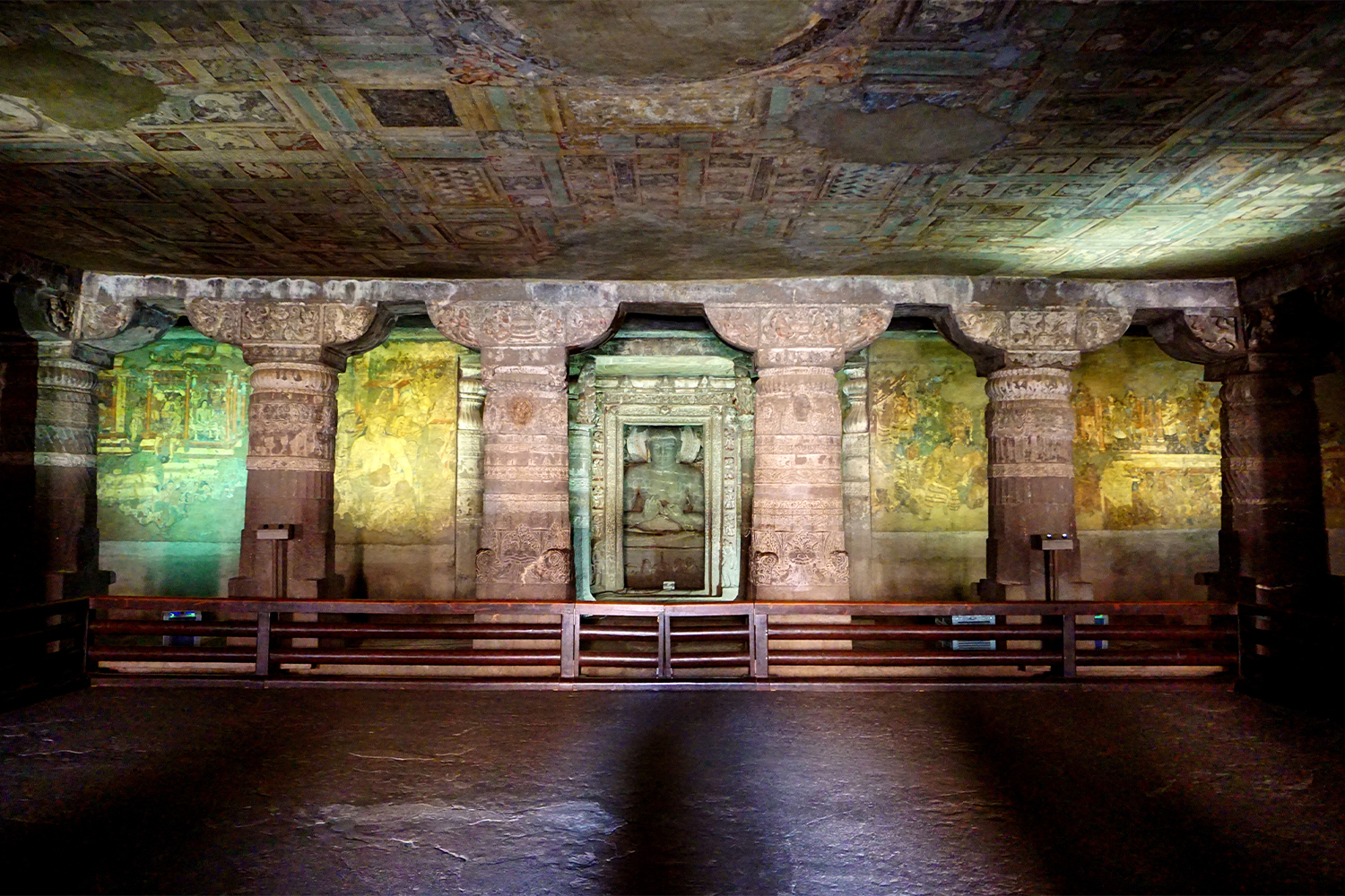 Photograph of the main shrine of Ajanta Cave 2 showing painted ceiling and walls and a statue of a seated Buddha in the middle