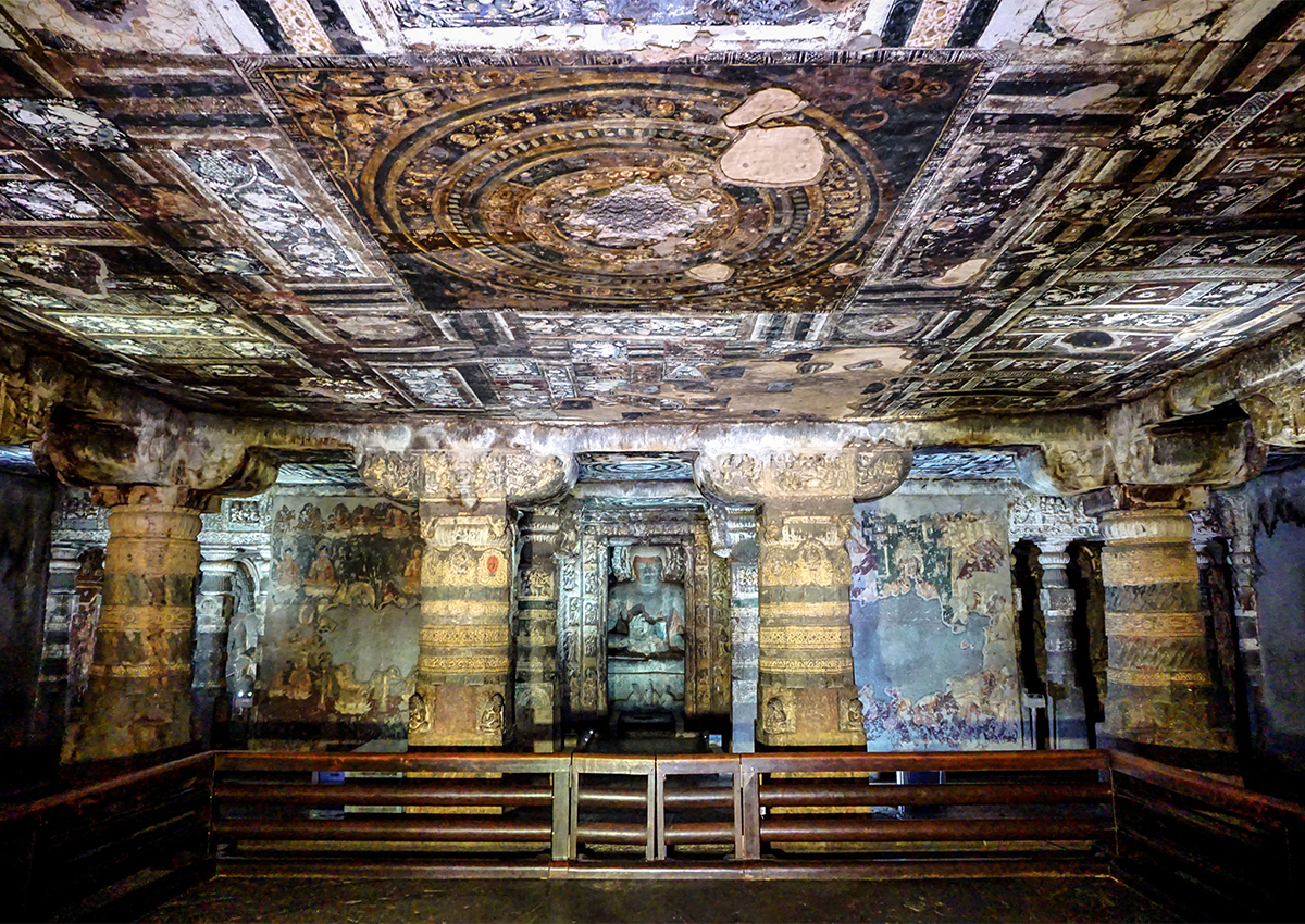 Photograph of the main shrine of Cave 2 at Ajanta Caves, with painted ceiling, walls and columns, statue of a seated Buddha at the far end