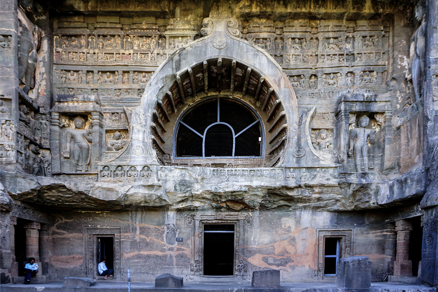 Photograph of the exterior of Ajanta Cave 26 showing doorways and large chaitya arch surrounded by relief carvings