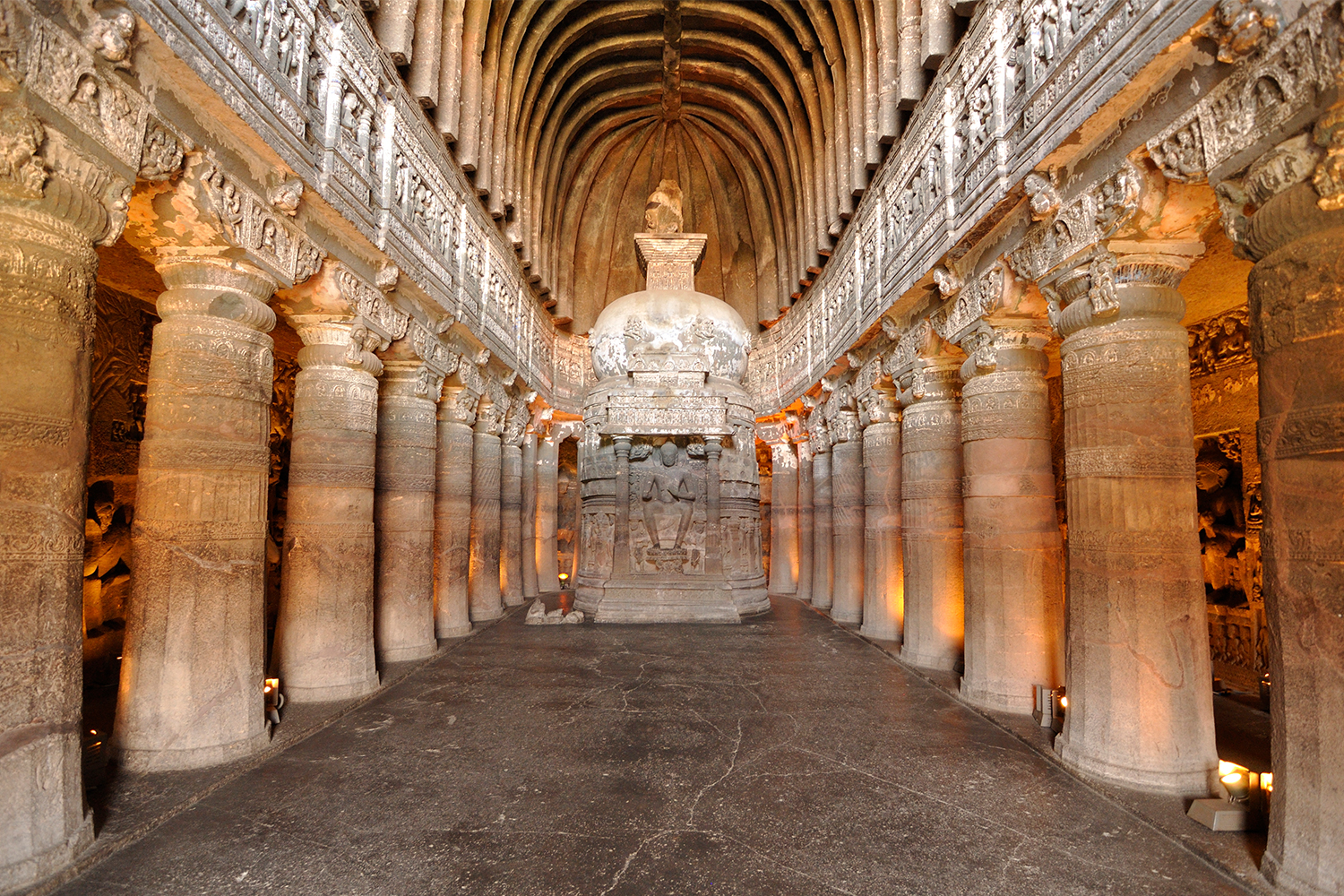 Photograph of the interior of the collonaded chaitya hall at Ajanta Cave 26 with a stupa bearing a relief carving of a seated Buddha