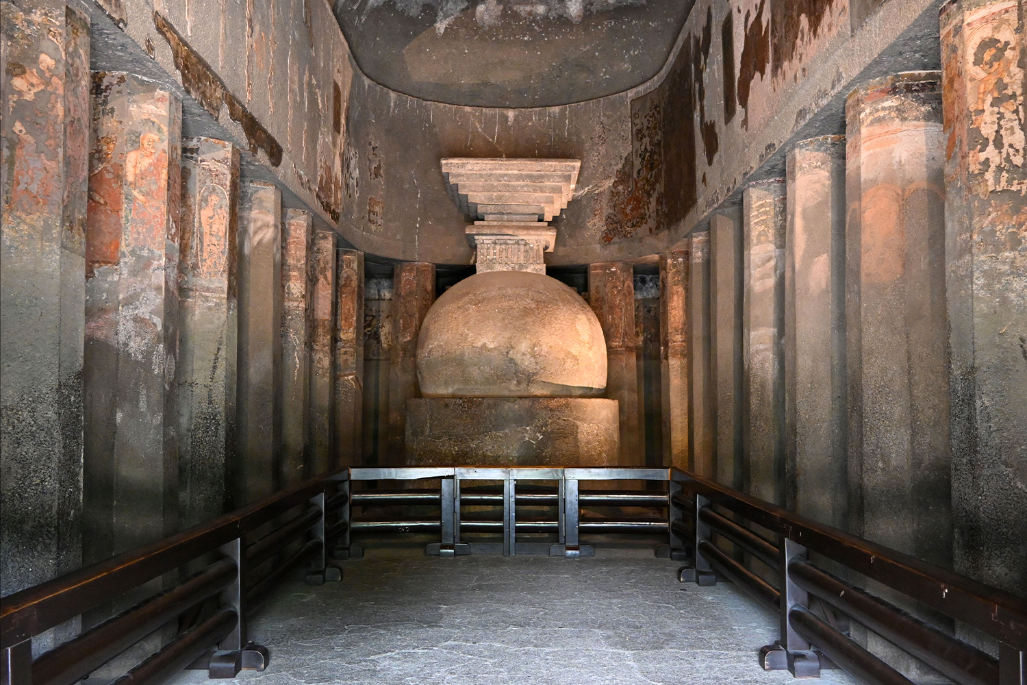 Photograph of interior of the chaitya hall at Ajanta Cave 9, with a plain stupa and lined with columns with mural fragments