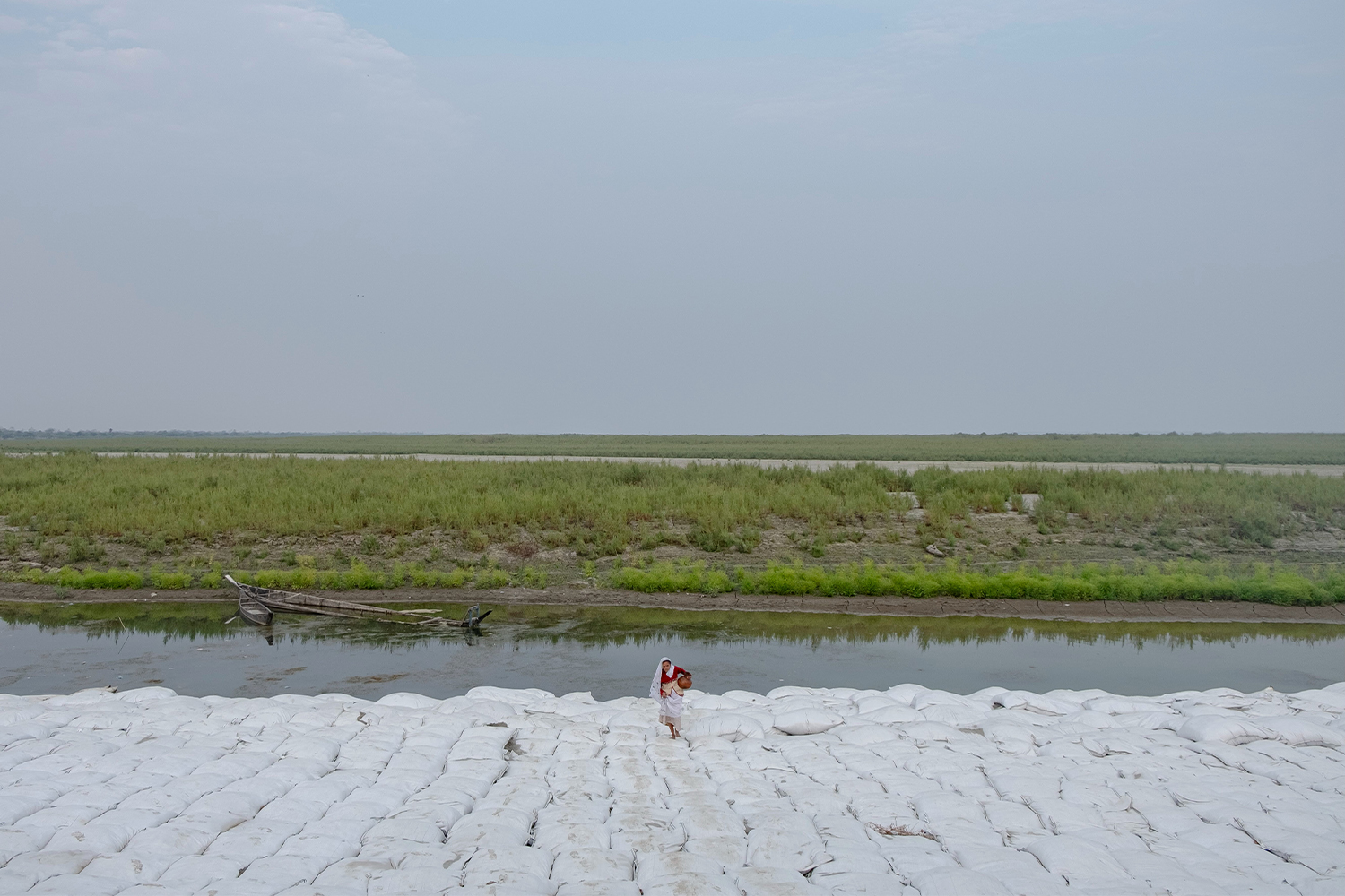Photograph by Kunga Tashi Lepcha showing a woman with a water pot walking over a mass of geotextile bags along the Brahmputra River