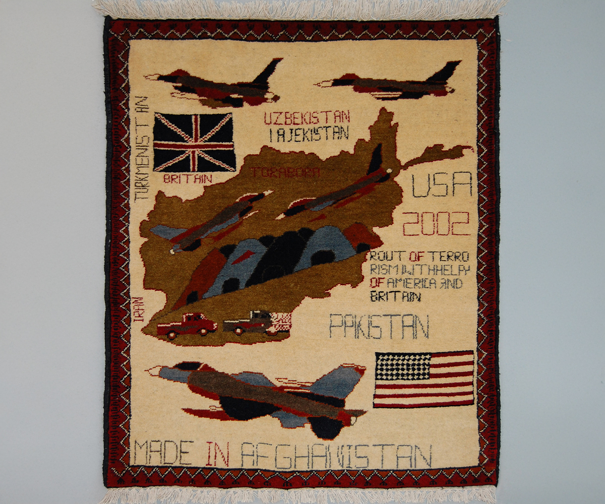 Beige war rug with Afghan map showing Tora Bora caves and fighter jets, with UK and US flags and English text, in dark red border