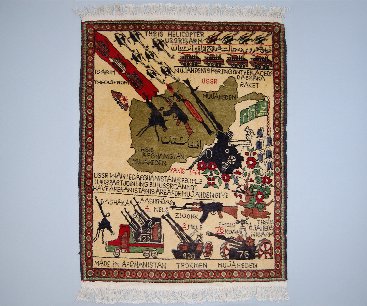 Beige rug showing map of Afghanistan with rocket launchers and rifles pointed at armoured vehicles and helicopters; flowering plant; and English text