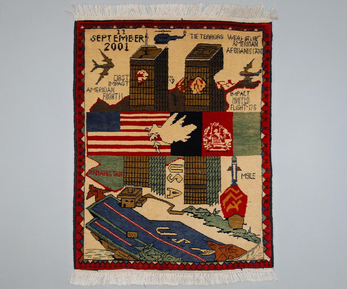 Beige coloured Afghan war rug with red borders depicting planes flying into the Twin Towers, the US and Aghan flags, and English text