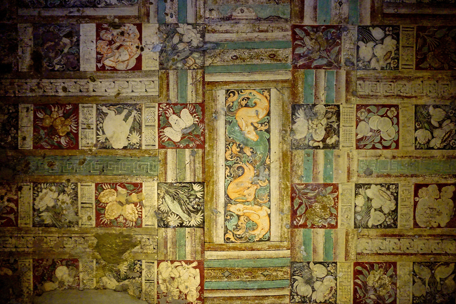 Photograph of ceiling mural in Ajanta Cave 1 showing a grid of animal, bird and human figures amidst floral patterns