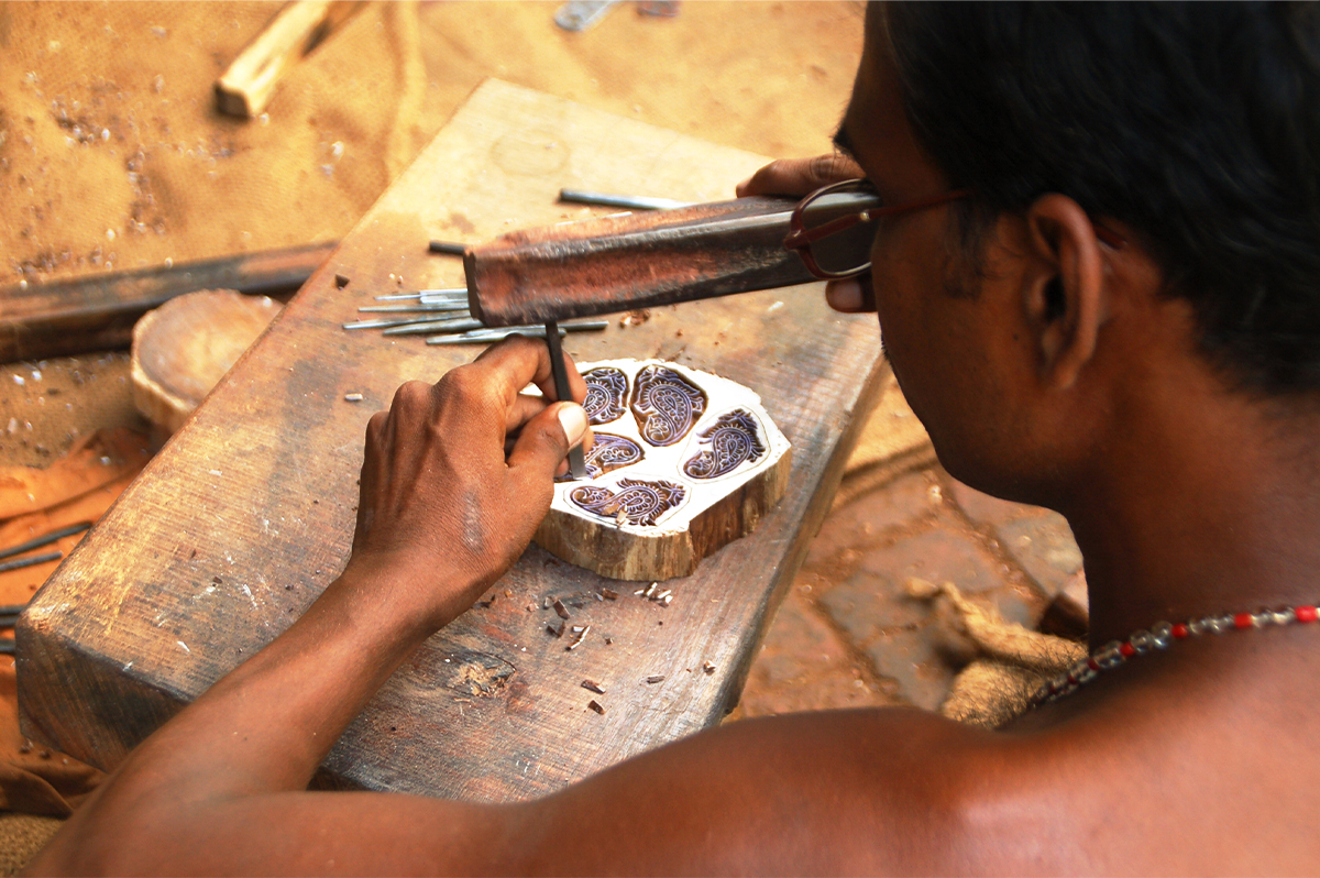 Photograph of an artisan carving a wooden block using a makeshift hammer and chisel