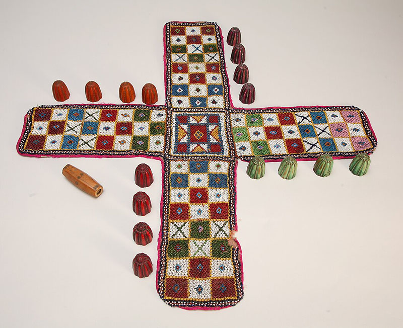 Photograph of a pachisi board game with players and a dice
