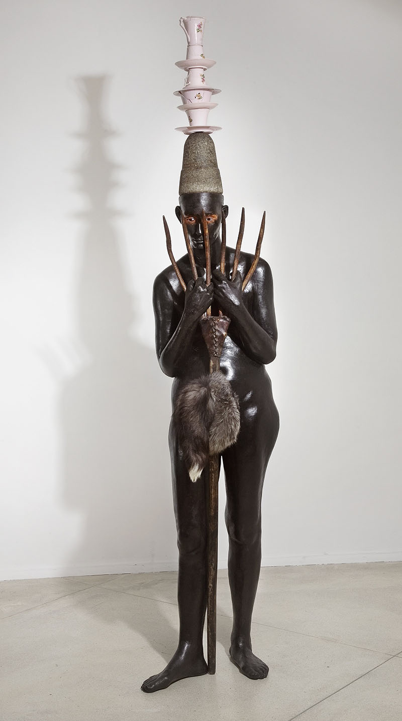 Mixed-media sculpture 'Lady with an Ermine' by Bharti Kher, showing a nude woman painted black with teacups on her head, holding a pronged instrument