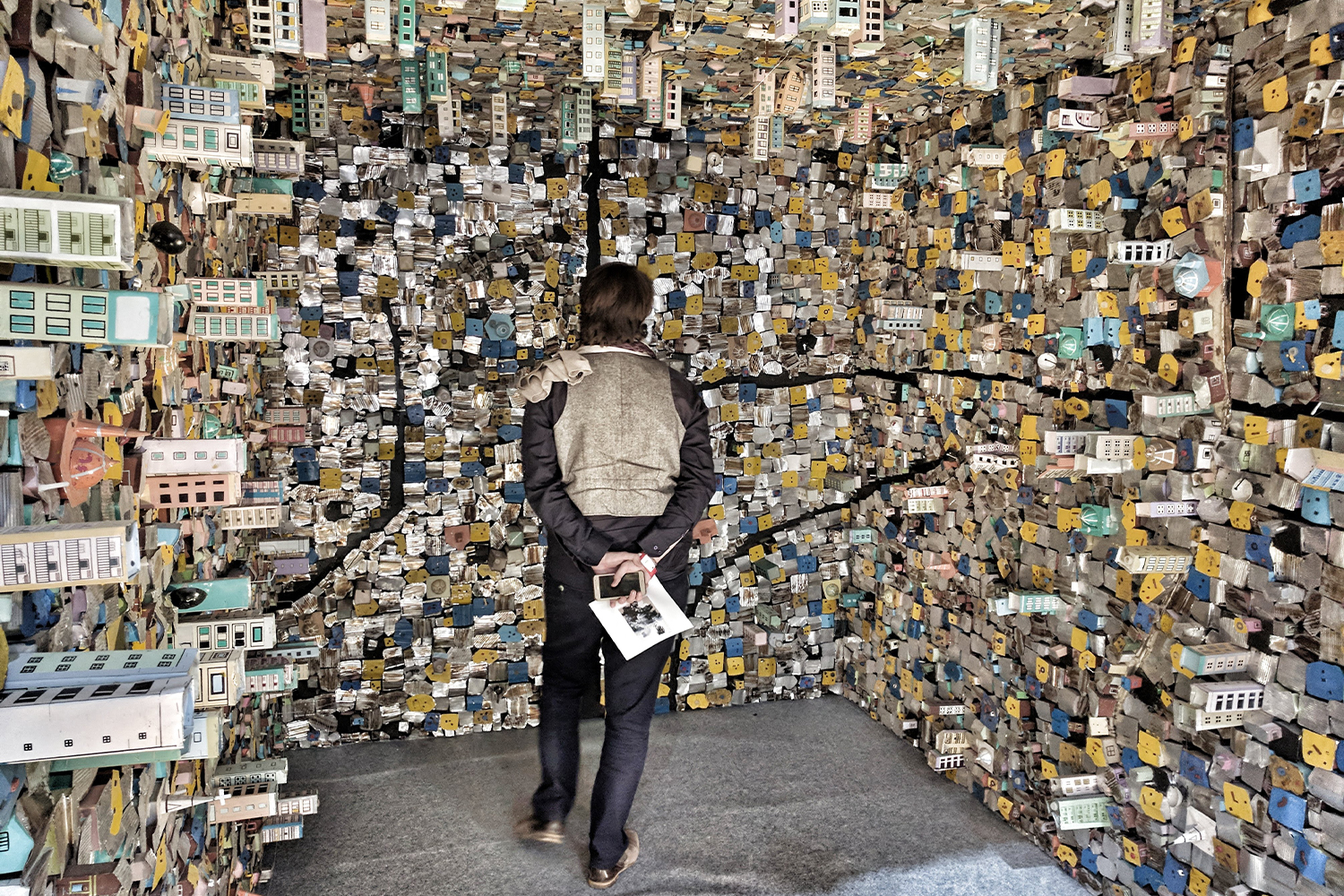 Photograph of a visitor viewing the installation '8' x 12'' by Hema Upadhyay, showing dense slum and buildings on three walls and ceiling