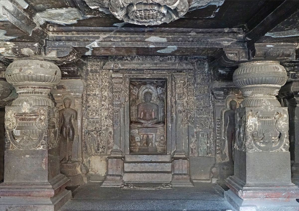 Photograph of the interior of the Indra Sabha or Ellora Cave 32 showing two pillars, two dwarapalas and a seated Mahavira in the sanctum