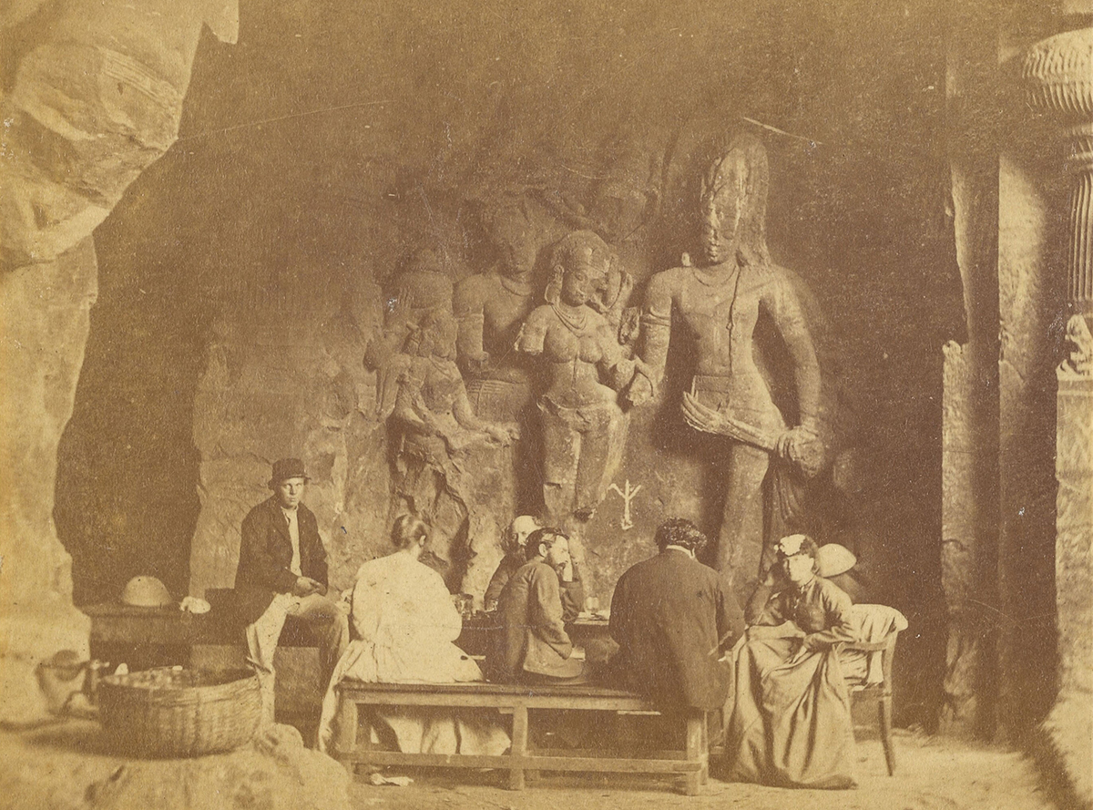 Monochrome albumen print showing a group of Europeans having a picnic in front of the Kalyanasundara relief sculpture at Elephanta Cave 1