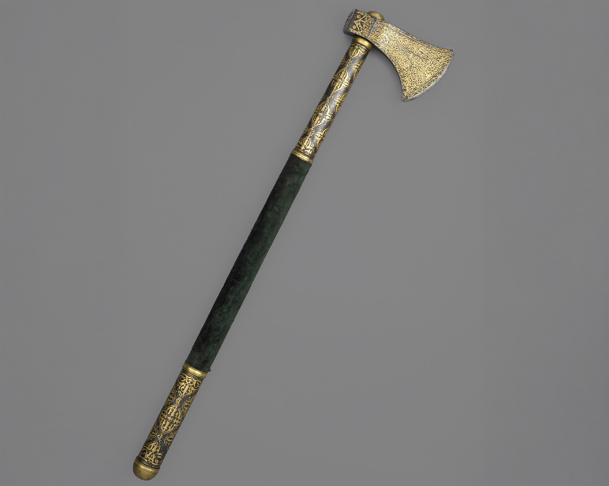 Photograph of a 19th-century steel battle axe with gold koftgari on its blade and green velvet on its handle