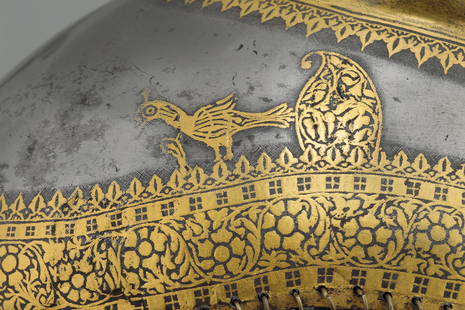 Close-up photograph of a Sikh helmet with a bird and other designs in gold koftgari