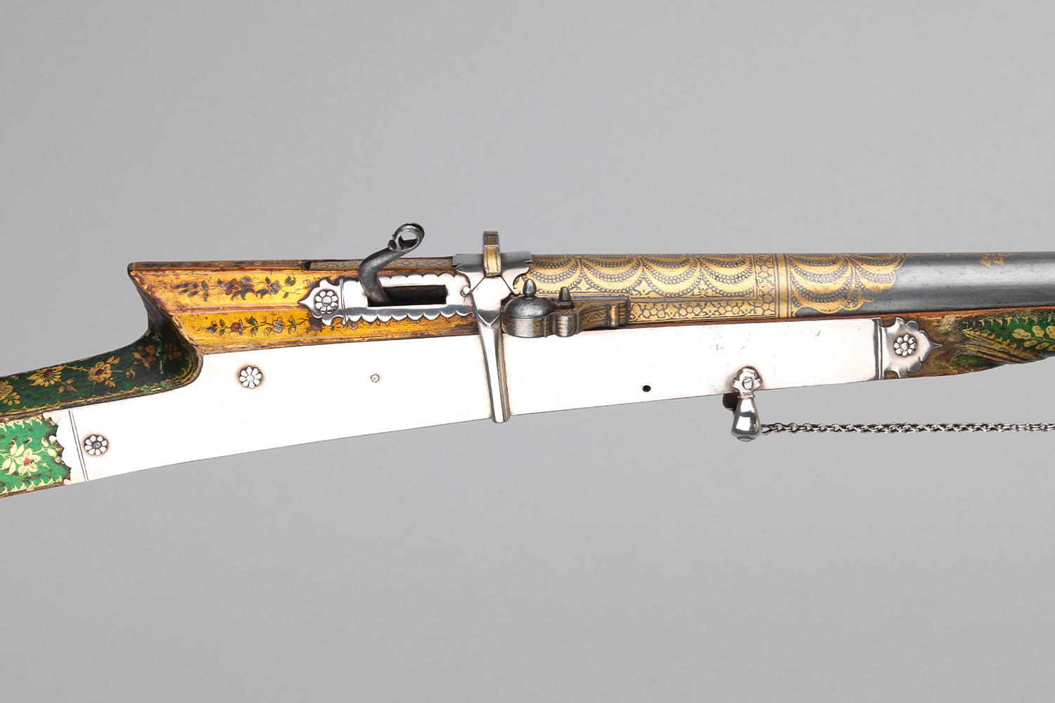 Close-up photograph of a 19th-century matchlock musket with green lacquer and gold koftgari on its barrel