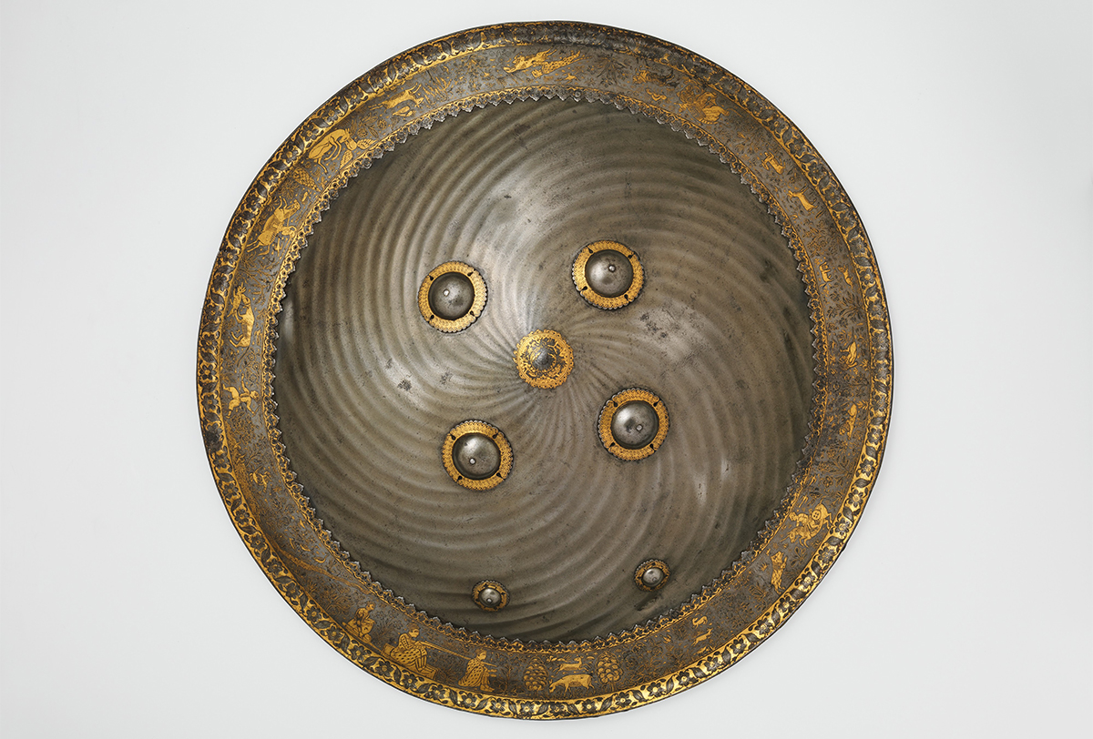 Photograph of a late 17th-century steel shield with gold overlay (koftgari) on its knob and rim showing hunting and landscape vignettes