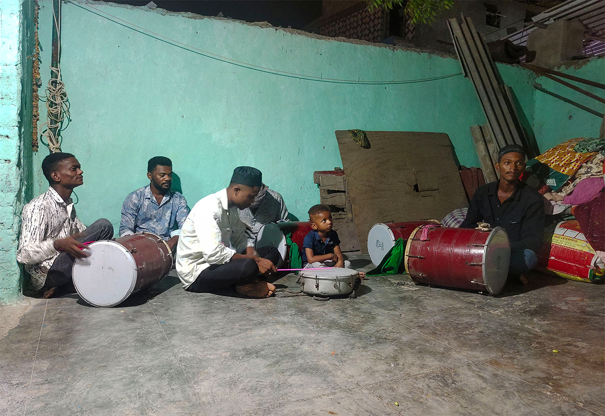 Photograph of a group of Siddi men sitting on the floor playing various musical instruments for baithaki dhamaal