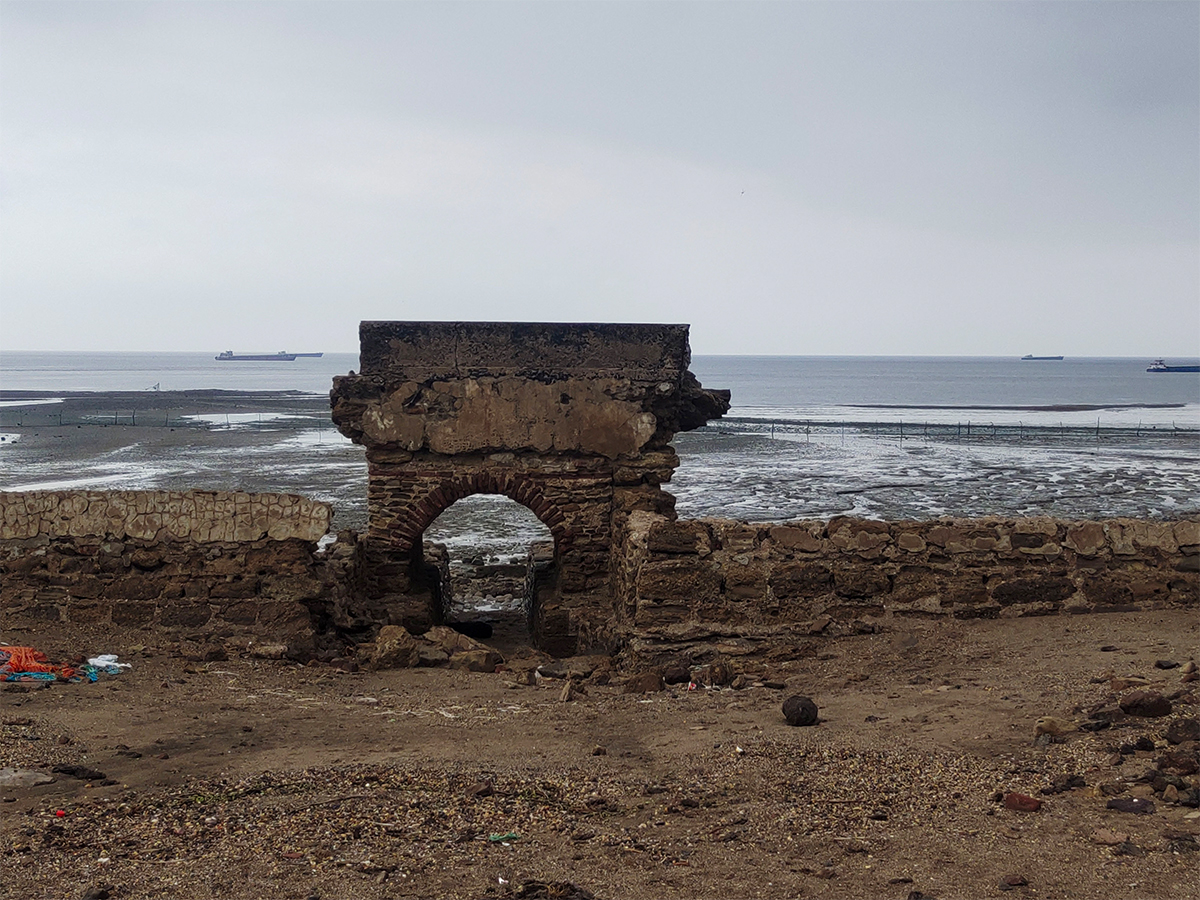 Photograph of a dilapidated Roman arch flanked by low wall overlooking the sea at Kuda, Gujarat