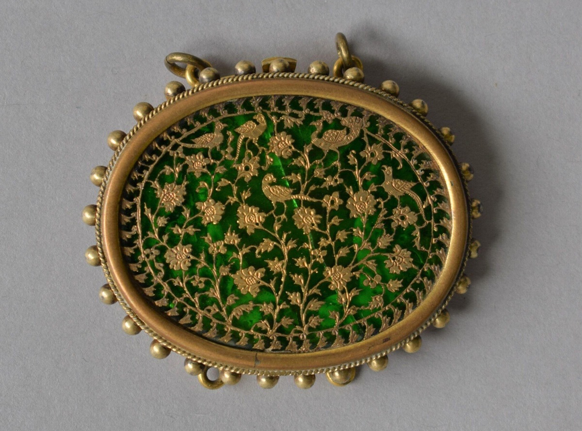 Photograph of an oval gilt silver pendant with beaded border and two suspension rings, inset with thewa work on green glass showing birds and flowers