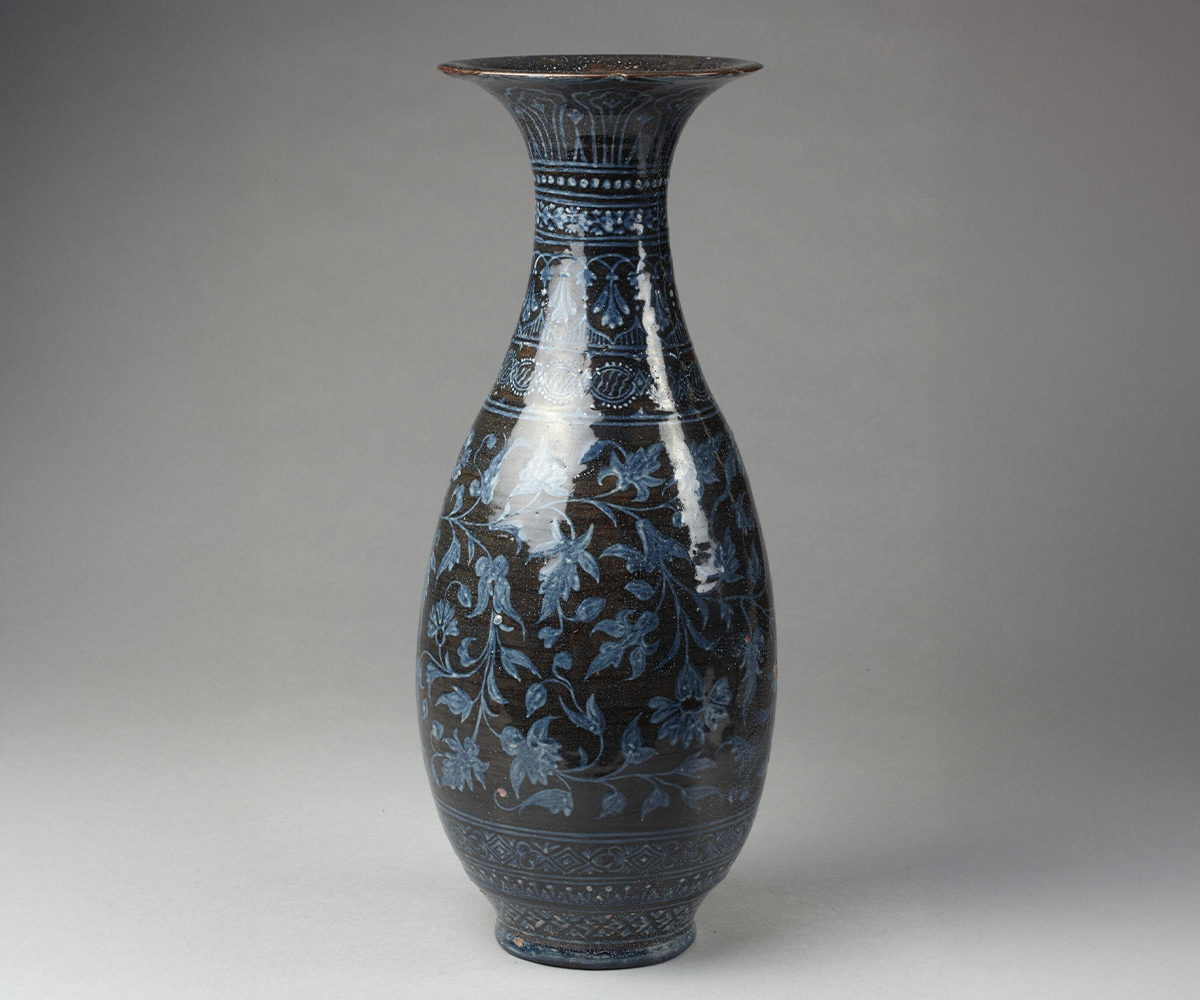 Photograph of a late-19th-century glazed ceramic vase decorated with flowering plant designs in a bluish grey on a dark grey background