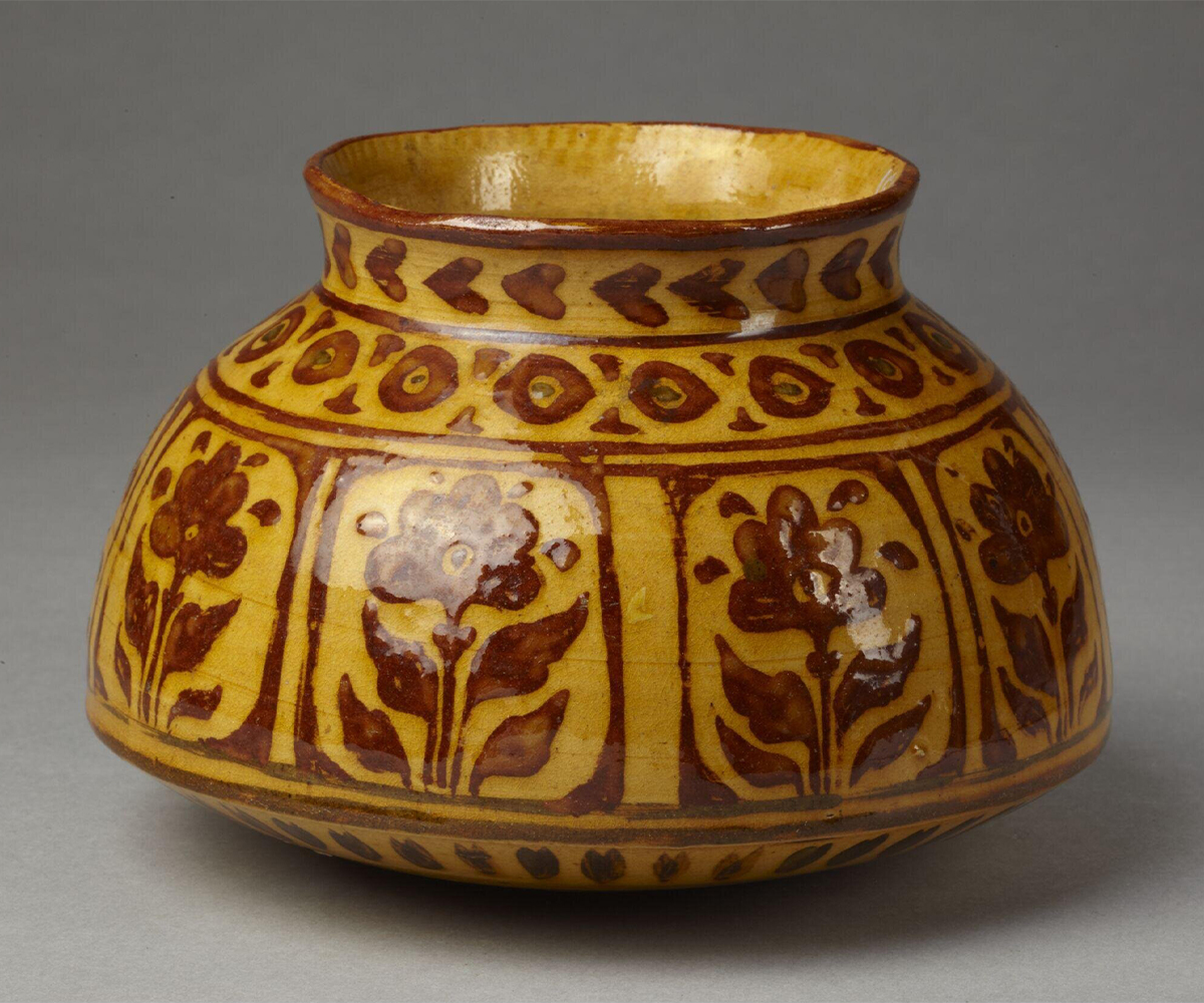 Photograph of a 19th-century glazed ceramic pot made by Ram Prasad, decorated with floral designs in red over a dark yellow background