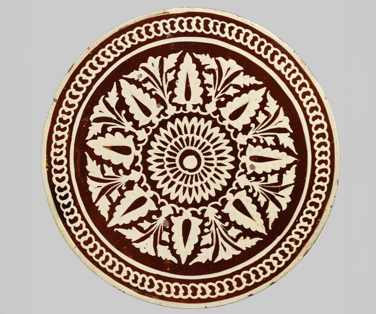 Photograph of a glazed earthenware dish decorated with a central rosette with radiating palmettes and border of interlocking circles in white over a brown background