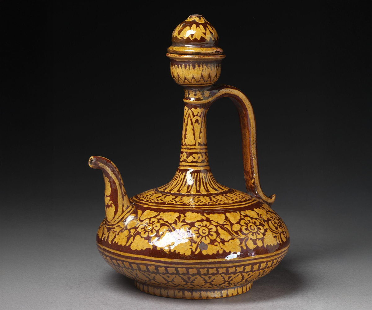 Photograph of a late-19th-century glazed ewer and lid with horizontal bands of stems, petals and leaves in yellow on a reddish background