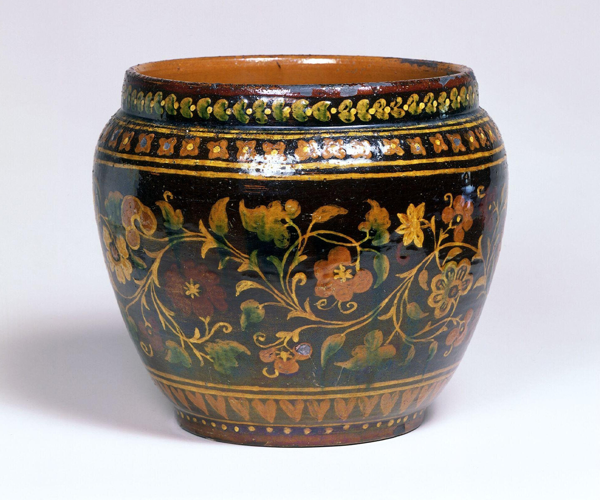 Photograph of a late-19th-century bowl decorated with multicoloured floral designs and other elements on a dark background