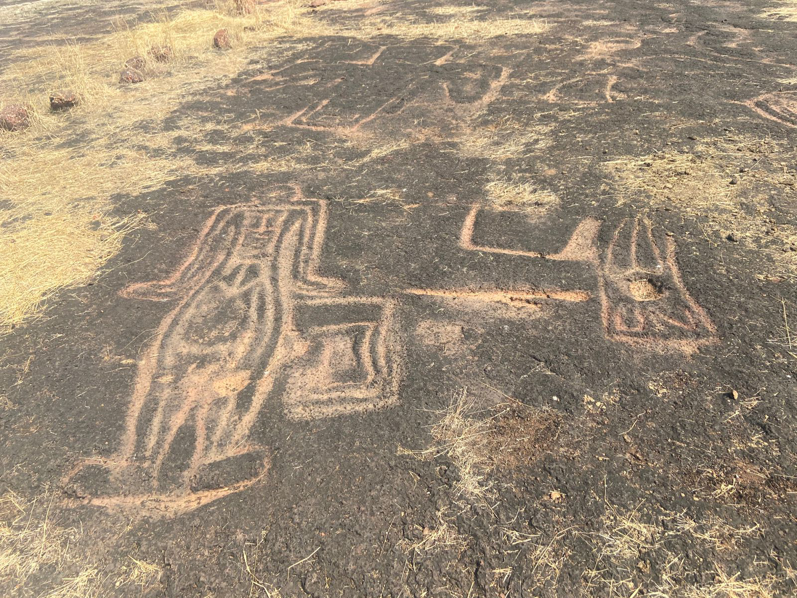 Photograph of petrogylphs at Kolambe showing a human like figure and other shapes