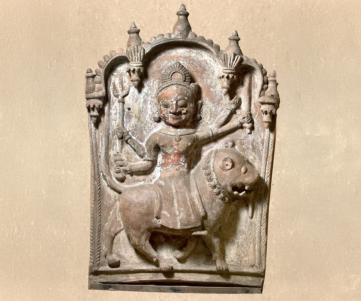 Photograph of a votive plaque of four-armed Durga riding a lion made out of clay and donkey dung