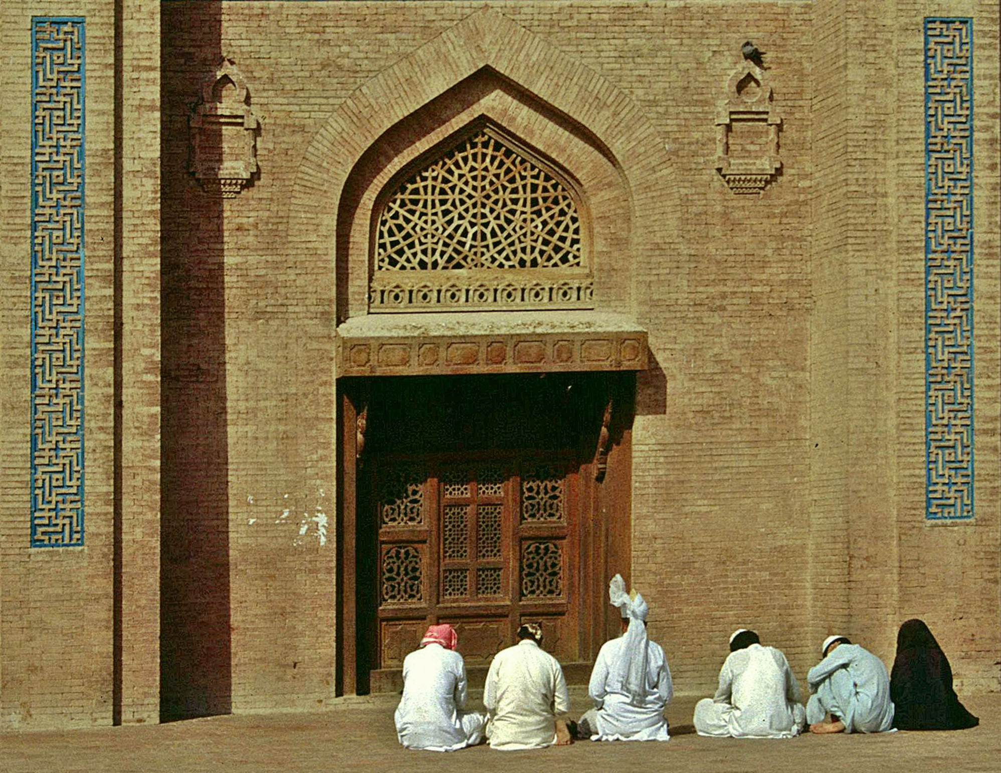 Photograph showing devotees sat in front of the shrine of Baha al-Din Zikriya