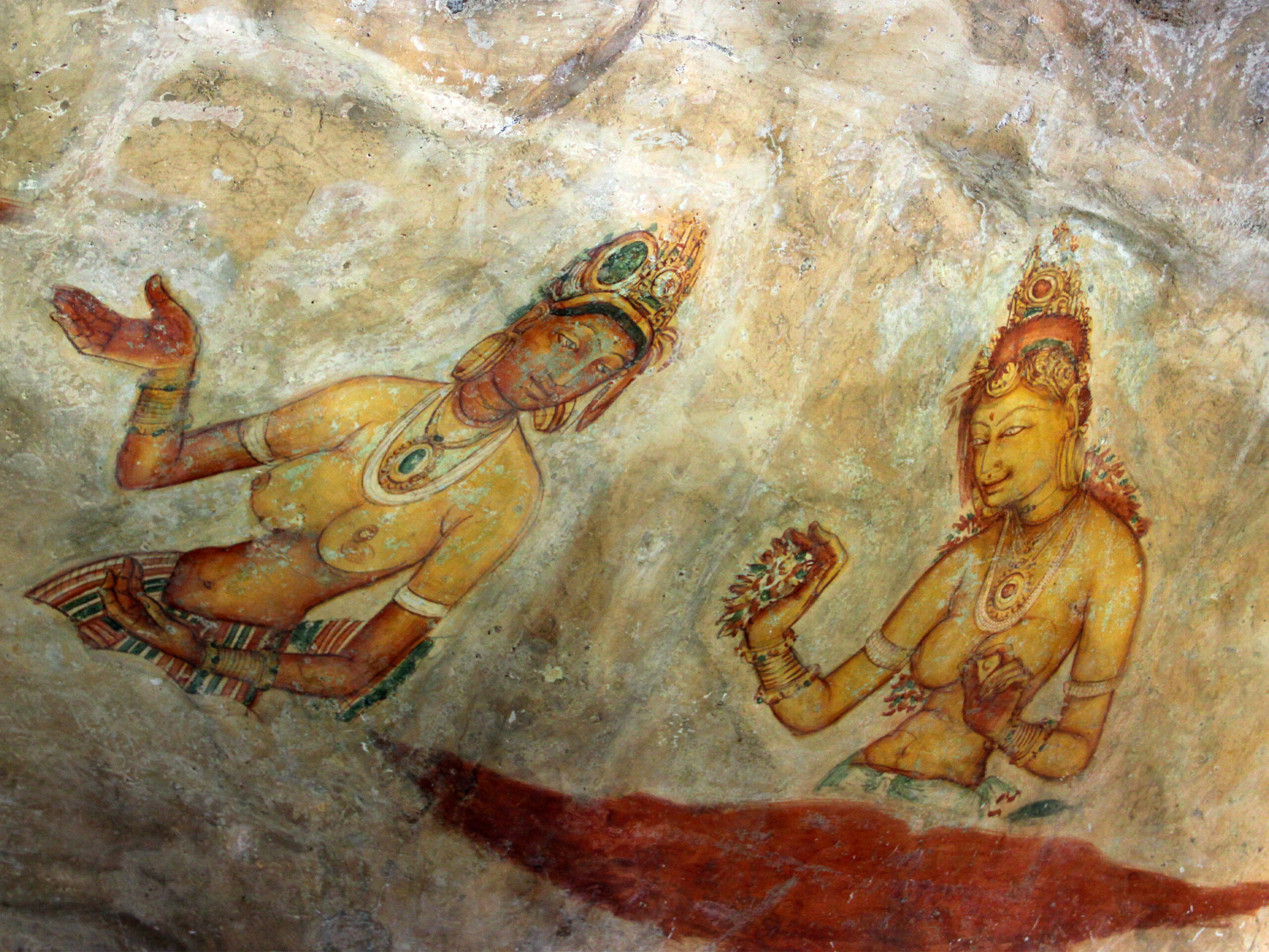 Photograph of a Sigiriya mural showing two bare-bodied heavily bejewelled women with one of them holding flowers in her hand