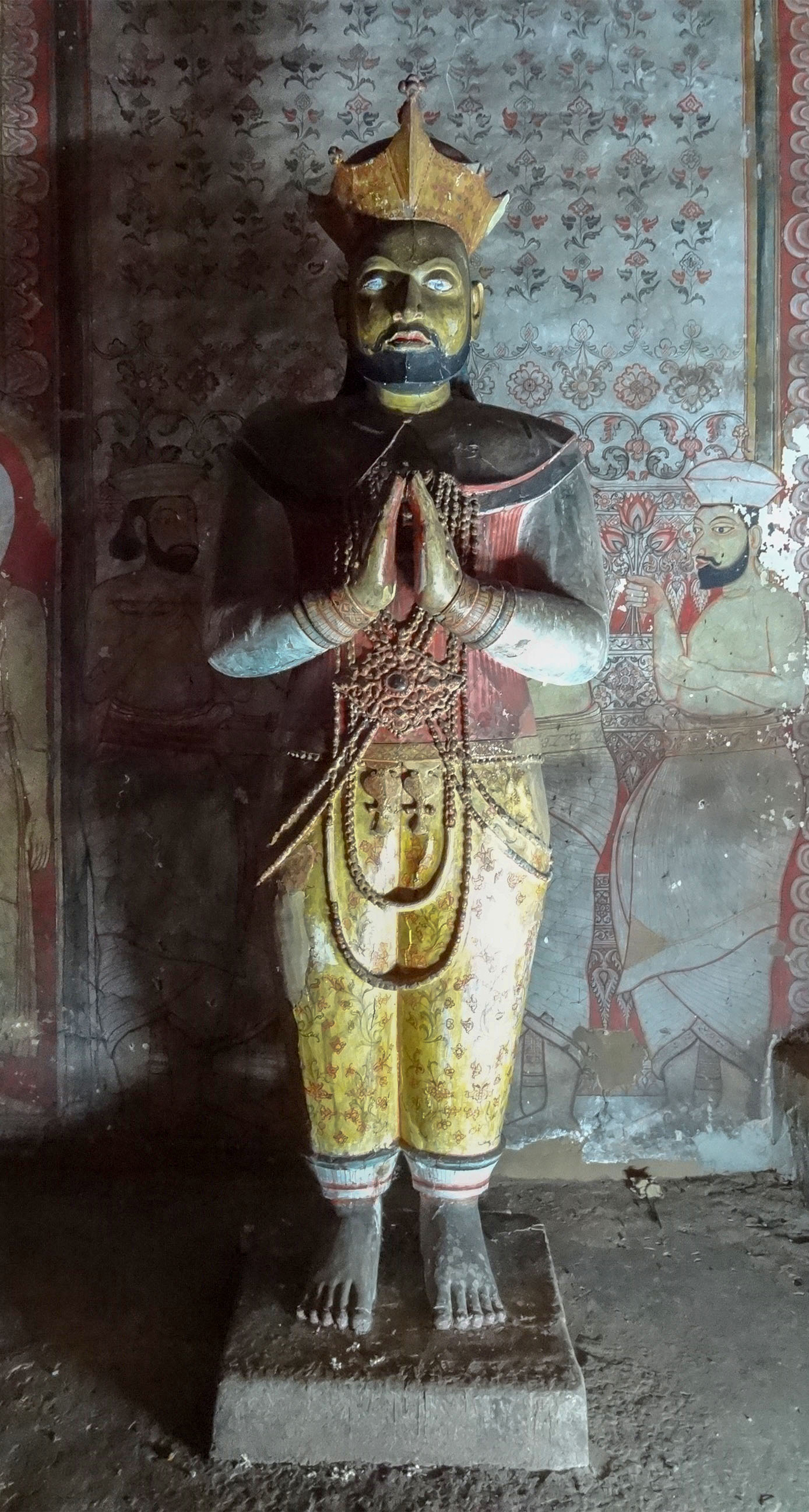 Photograph of a staue of a king with its hands joined together in anjali mudra inside the Dambulla Caves