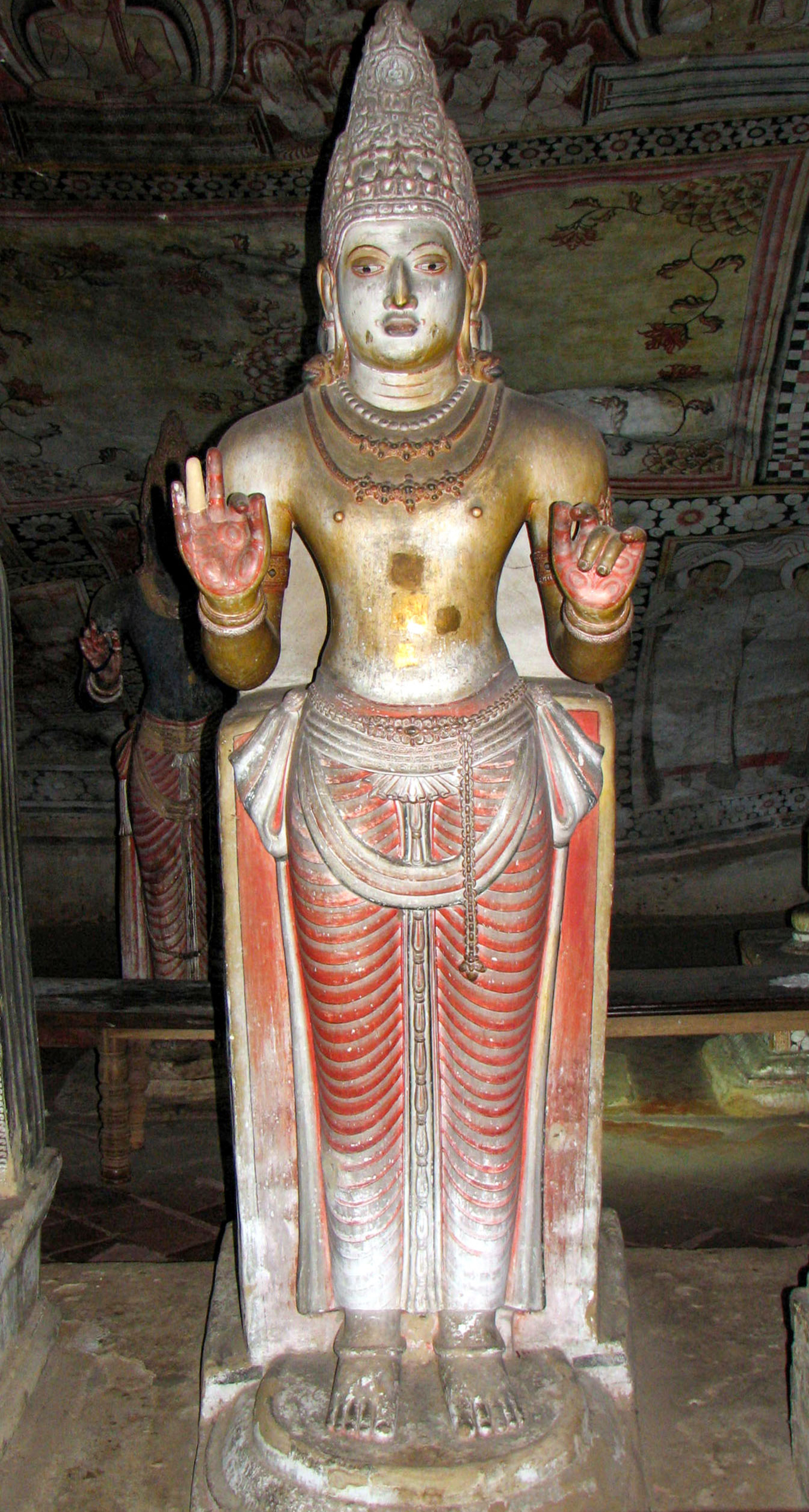 Photograph of a Buddhist or a Hindu deity with its left hand raised in the vitarka mudra and the right hand in the karana mudra inside the Dambulla Caves