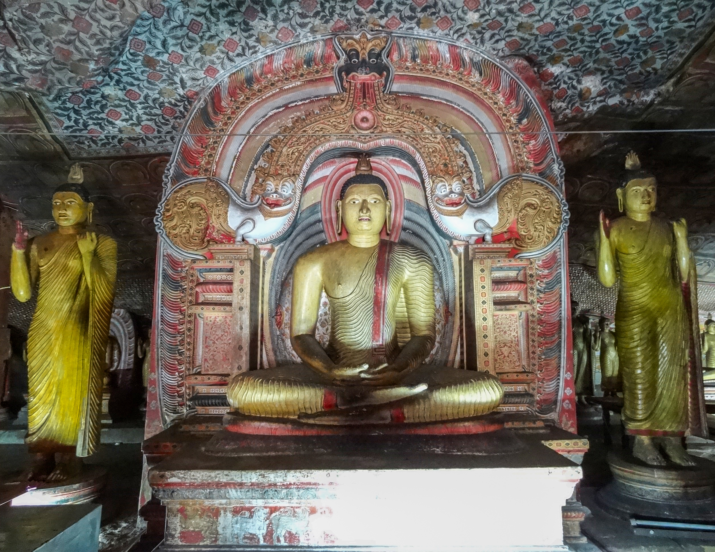 Photograph of a seated Buddha flanked by two other Buddhas or Bodhisattvas inside the Dambulla Caves