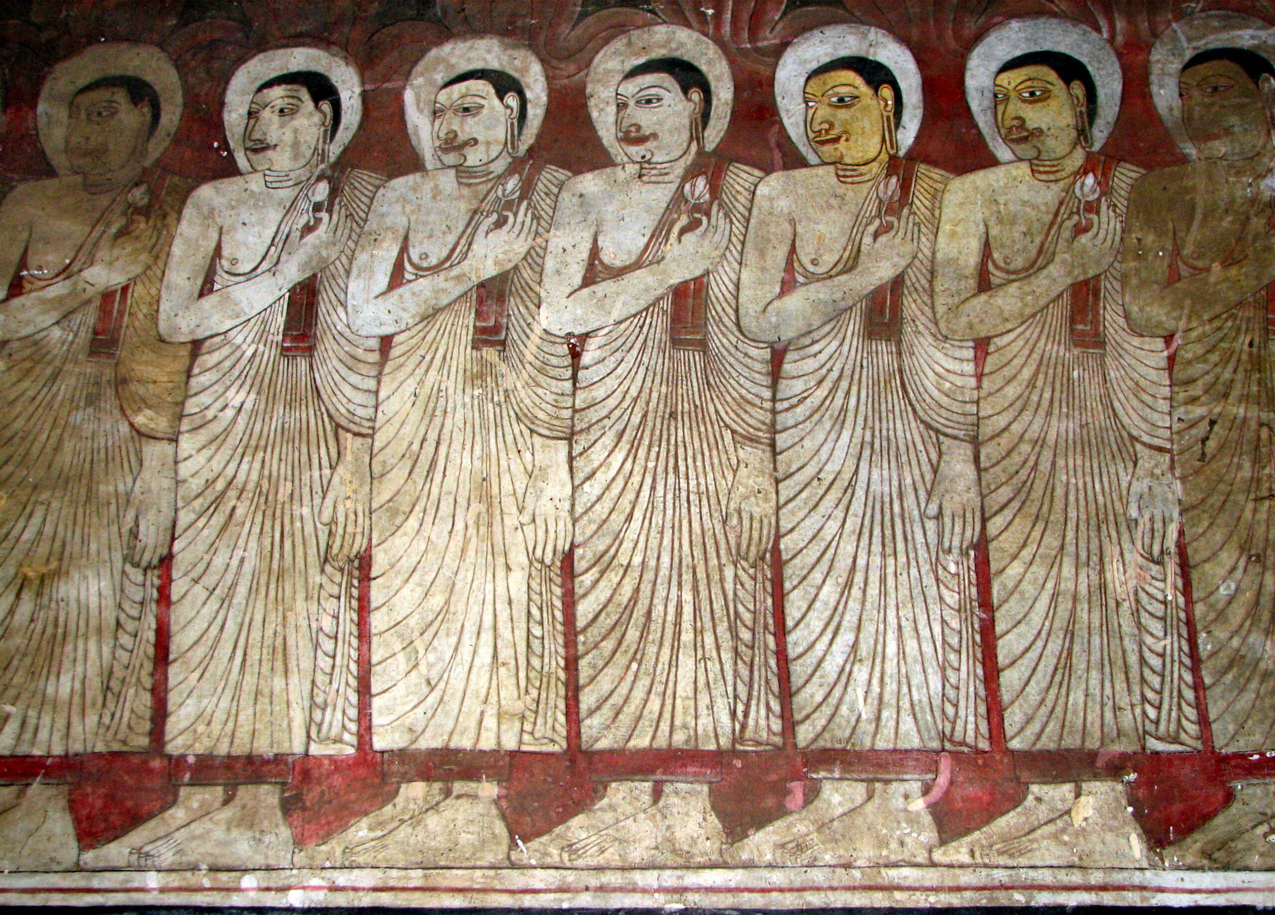 Photograph of a mural inside the Dambulla Caves showing multiple standing Buddhas dressed in white cloaks with halos holding a lotus