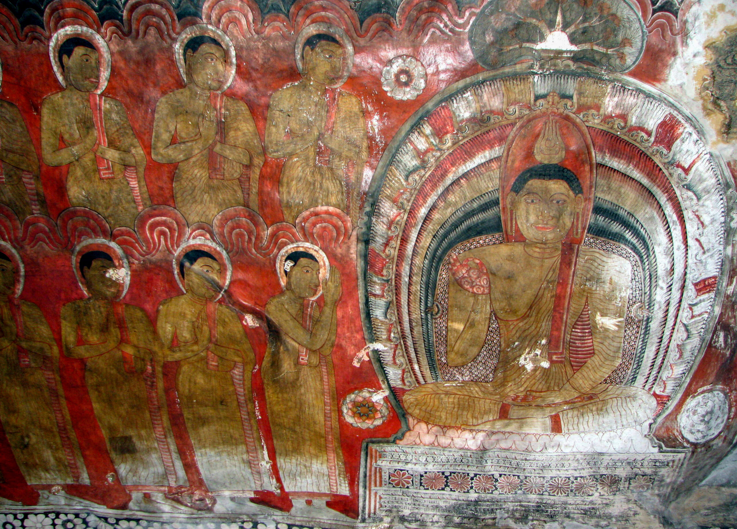 Photograph of a mural inside the Dambulla Caves showing a seated Buddha flanked by devotees