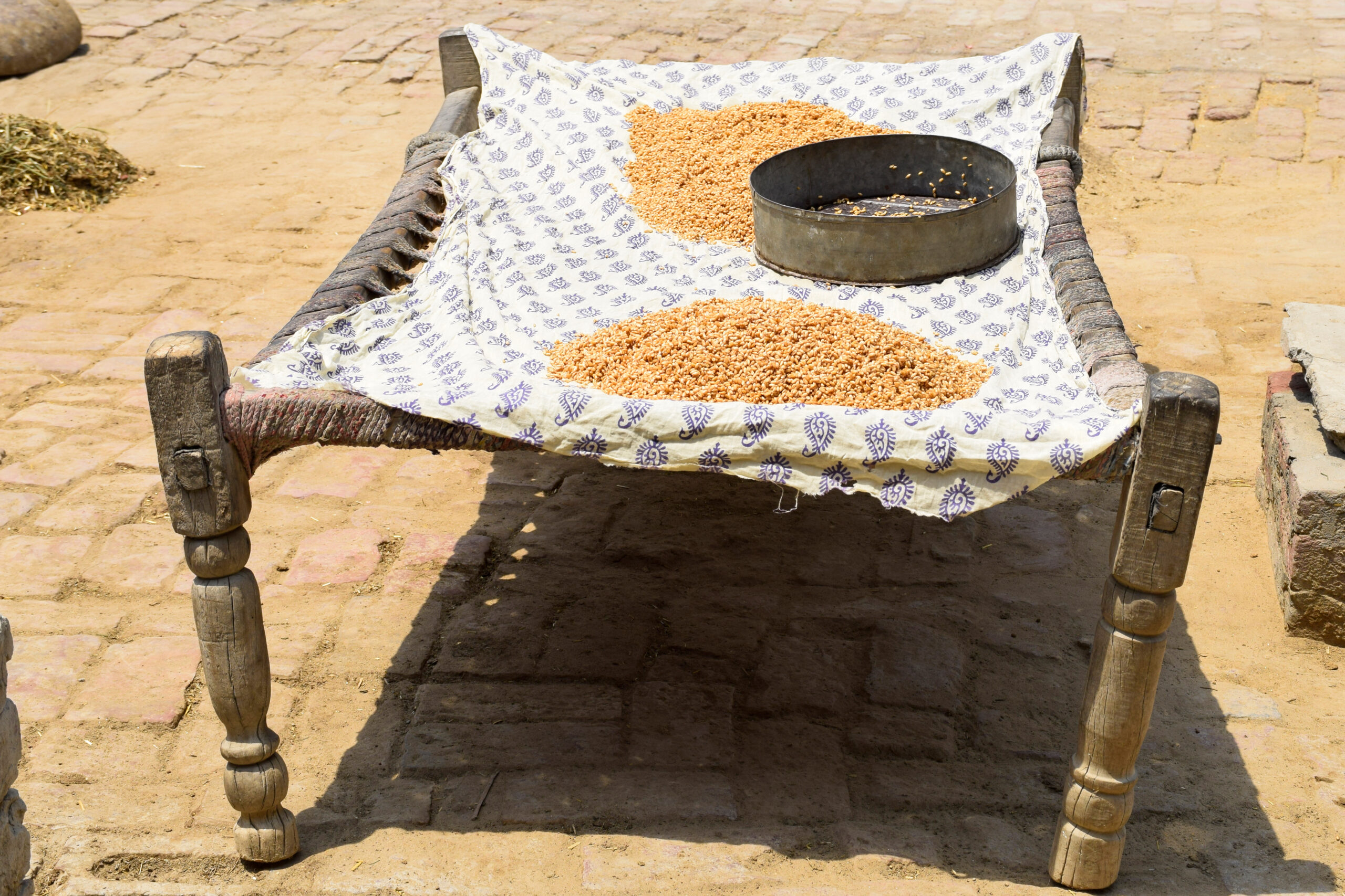 Photograph of a charpoy being used for drying grains in the courtyard of a house