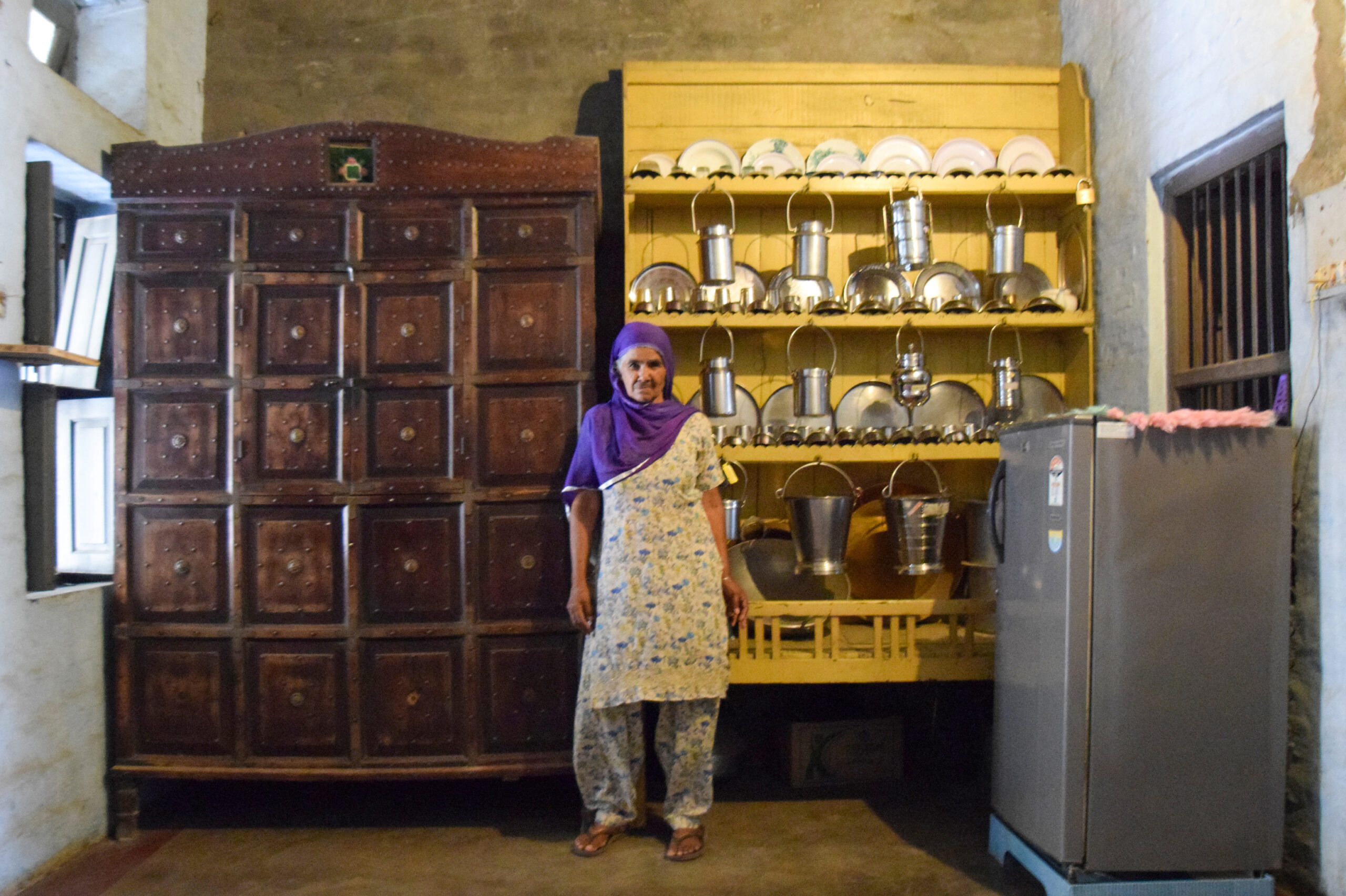 Photograph of a lady named Manjeet Kaur standing in front of the sandook that she was given by her family