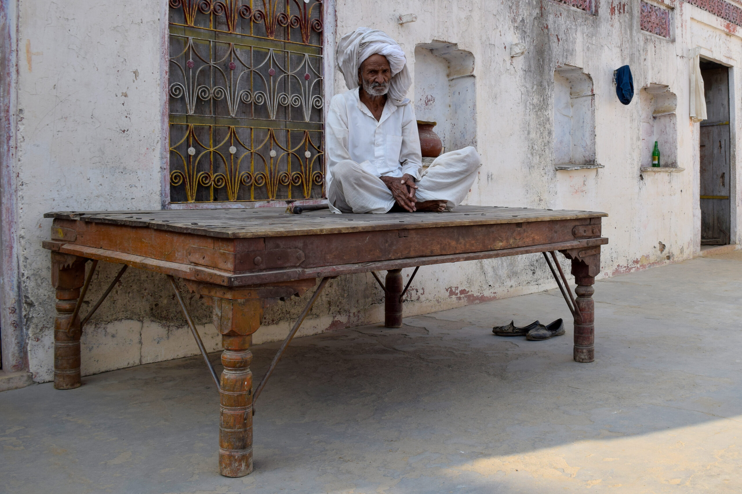 Photograph of a man seated on a takhat in a village home in Haryana
