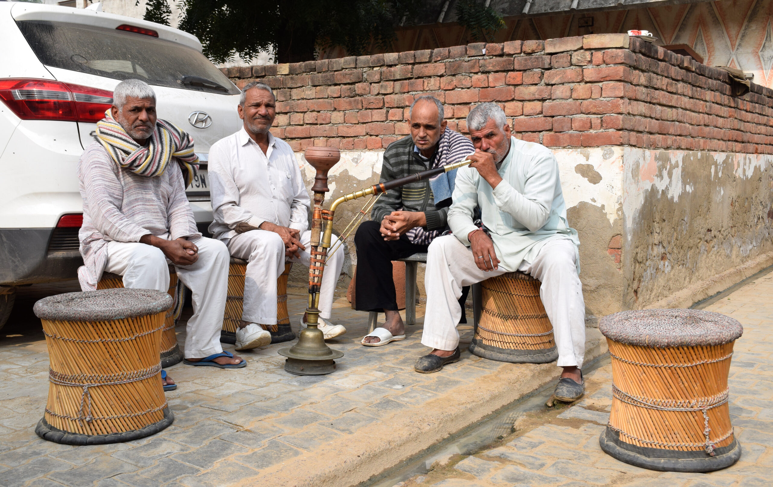 Photograph of a group of men seated on mudhas smoking a hookah