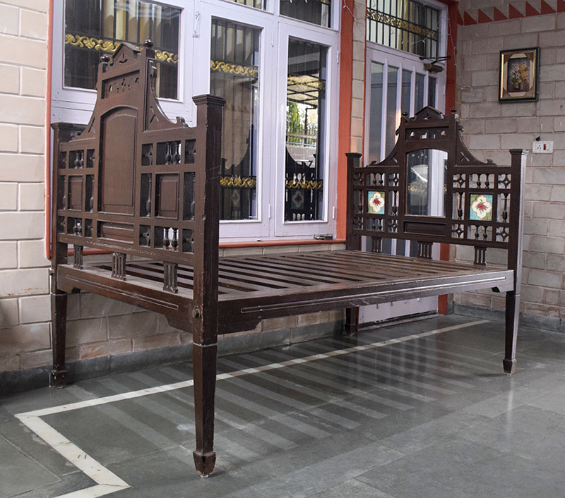 Photograph of a wooden bed called a palang decorated with a mirror and ceramic tiles